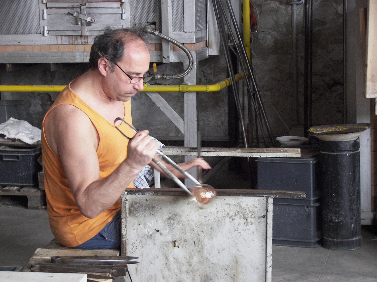 Glass master working molten glass at a Murano furnace during the commented glassmaking demonstration on the private boat tour