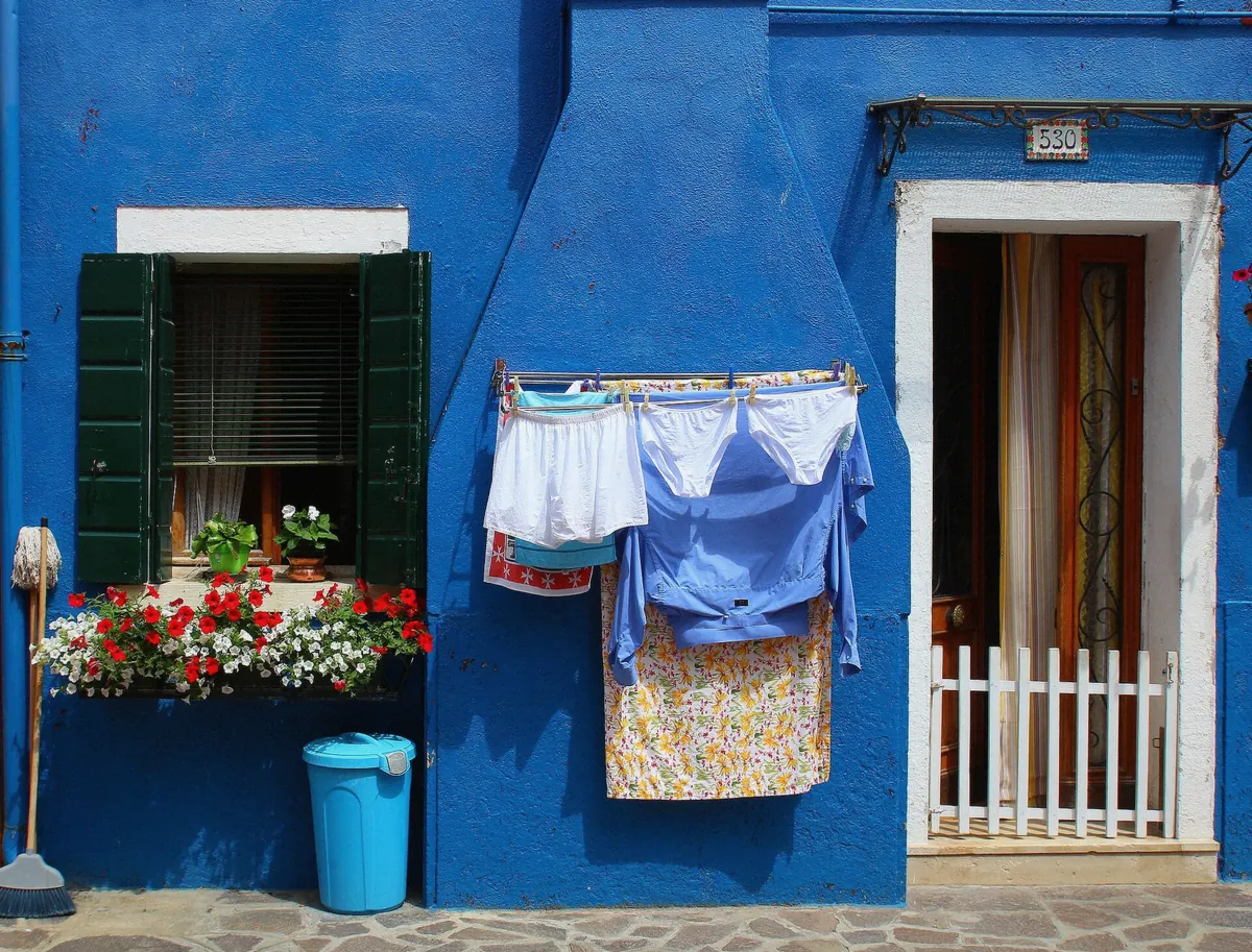 Laundry lines over a Burano canal between painted houses, the lived-in side of the island worth the trip